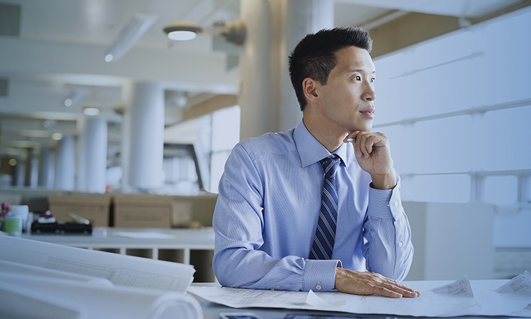 Man sitting at desk looking off in distance - Process Optimization by Jefferson Wells